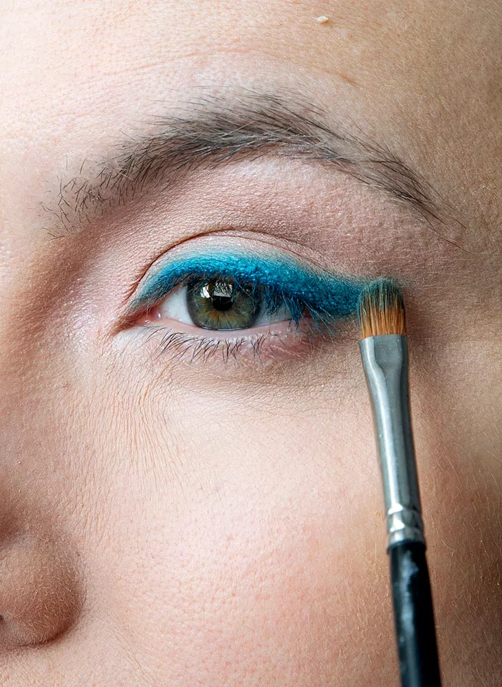 Värikäs meikki on trendikäs. Kuvassa malli lisää sinistä luomiväriä silmiin. 