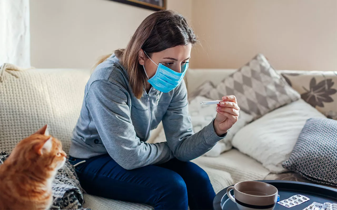 Nainen istuu sohvalla maski päässä. Koronaviruksen tarttuminen muihin voi pelottaa jopa enemmän kuin oma sairastuminen. 