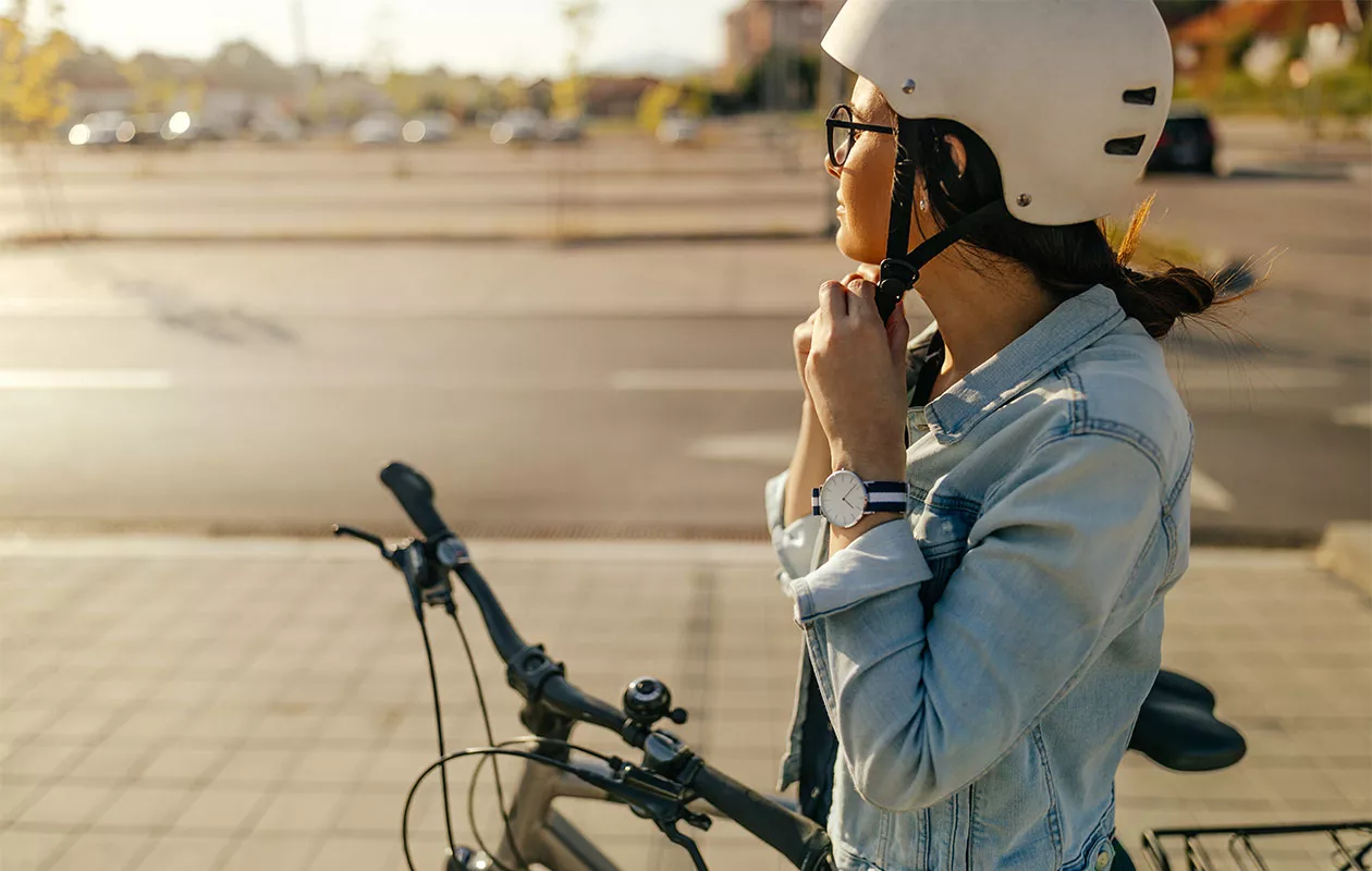 Nainen pyörän vieressä laittamassa kypärää kiinni. Pyöräilyn hyödyt riippuvat usein siitä, millaista matkaa polkee ja miten usein.