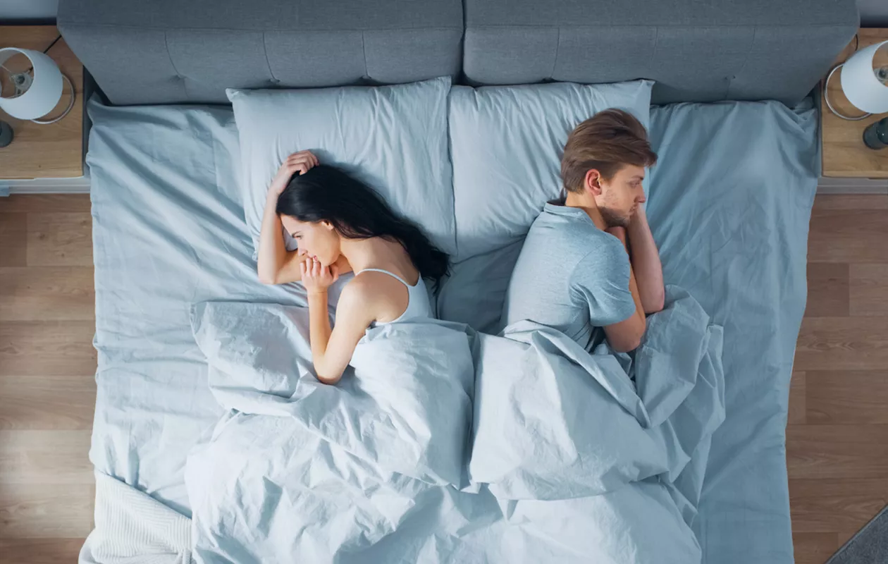 Mustasukkaisuus parisuhteessa: pariskunta makaa sängyssä surullisena.