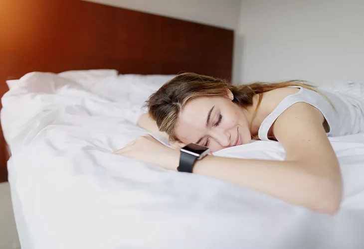 Älykellovertailu: eri valmistajien kellot eroavat esimerkiksi unen mittaamisen suhteen. Kuvassa nainen makaa sängyllä älykello kädessä.