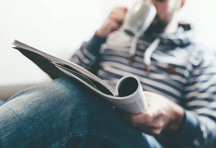 Tauko työpäivän aikana: mies lukee lehteä ja hörppii kahvia.