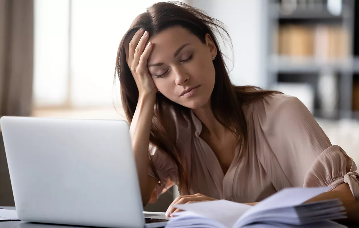 Nuori nainen istuu väsyneenä silmät kiinni tietokoneen edessä. Krooninen väsymysoireyhtymä eli CFS voi olla jopa niin vaikea, että haittaa normaalia elämää.