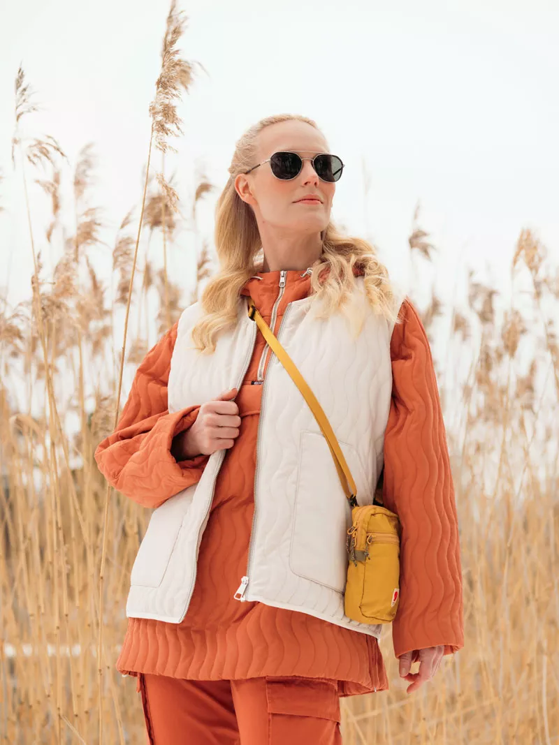 Nainen seisoo pellolla yllään oranssi tikkianorakki ja valkoinen tikkiliivi. 