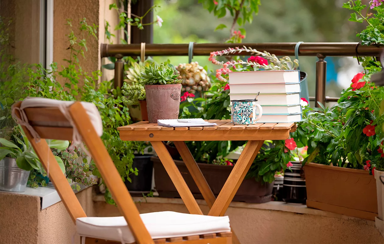 Kuva pienestä parvekepöydästä, jonka ympärillä on kasveja eri tasoilla. Parvekkeen sisustaminen on usein luovaa puuhaa.
