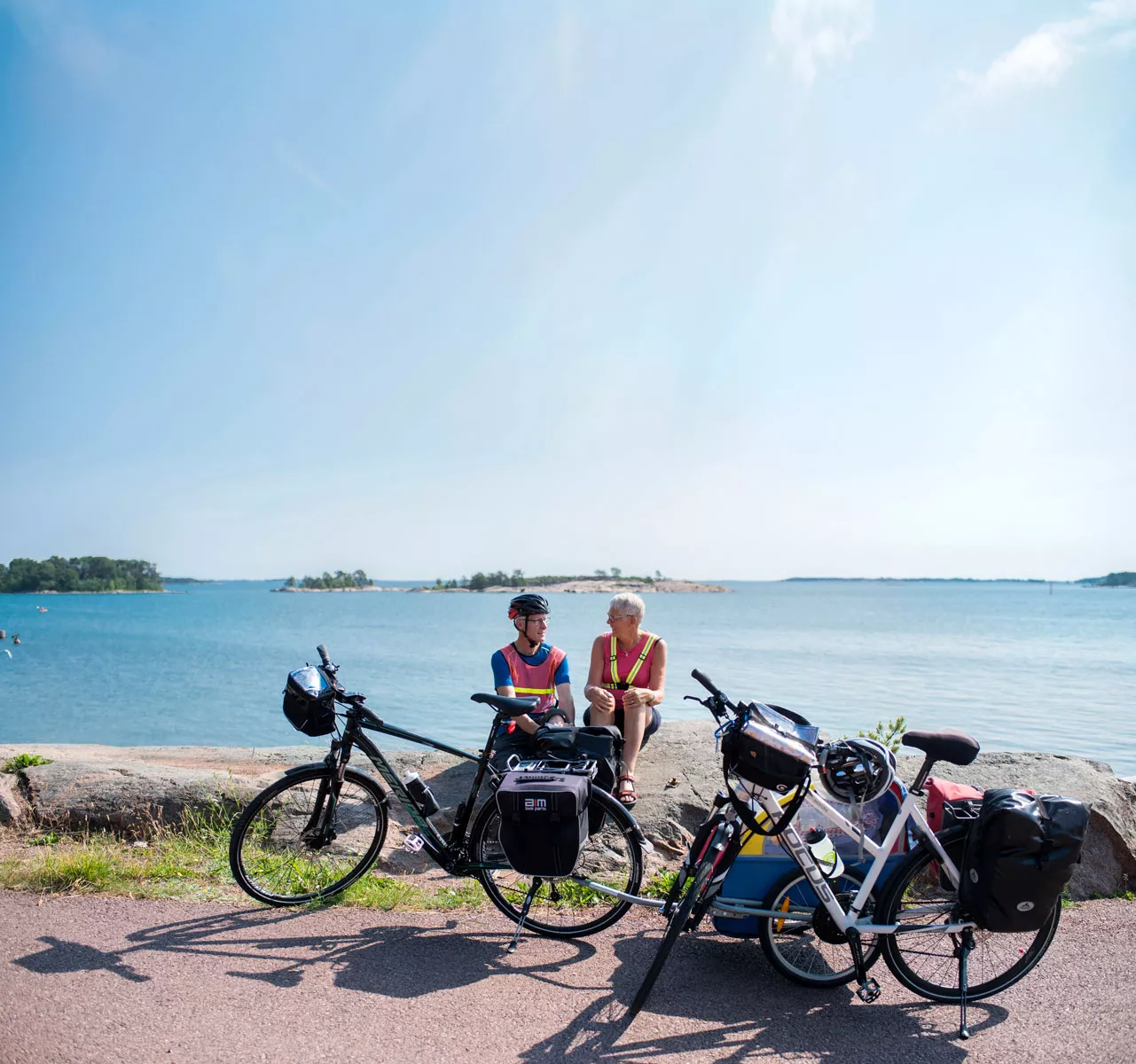 Kaksi ihmistä istuu  kallioilla meren äärellä edessään pyörät. Ahvenanmaa on erinomainen pyöräilypaikka.