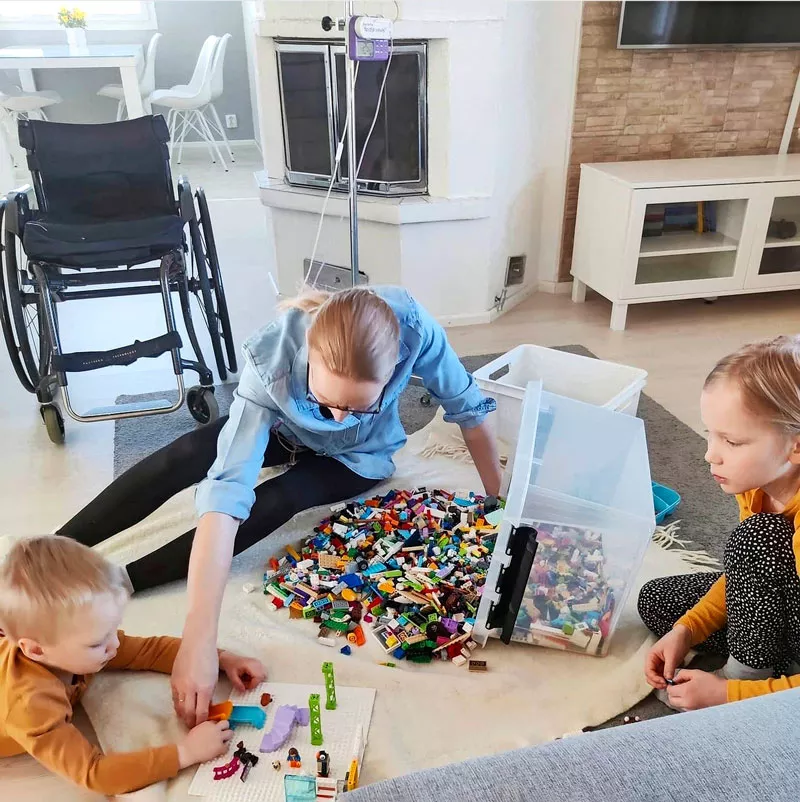 Sonja-Elina istuu olohuoneen lattialla ja rakentelee legoista lastensa Lennin ja Aadan kanssa.