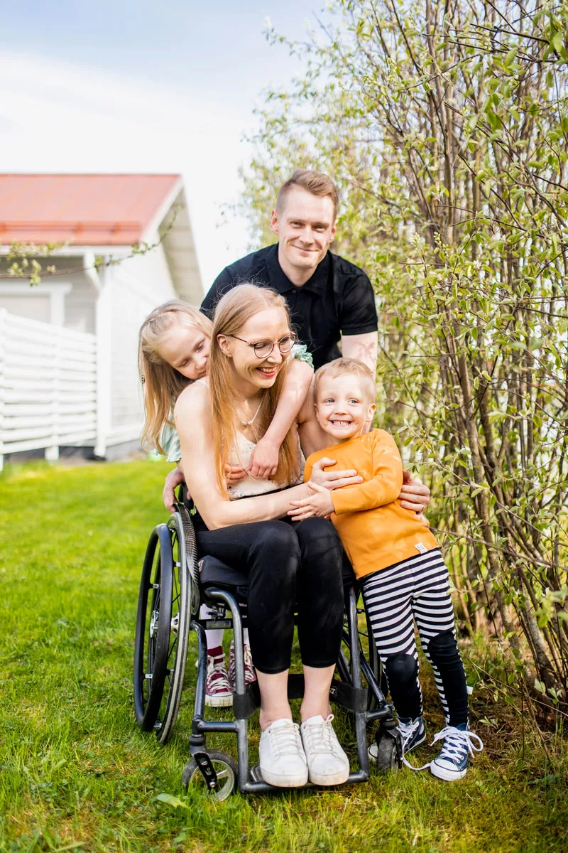 Sonja-Elina Tähtinen istuu pihalla pyörätuolissa ympärillään Jukka-puoliso ja lapset Aada ja Lenni. 