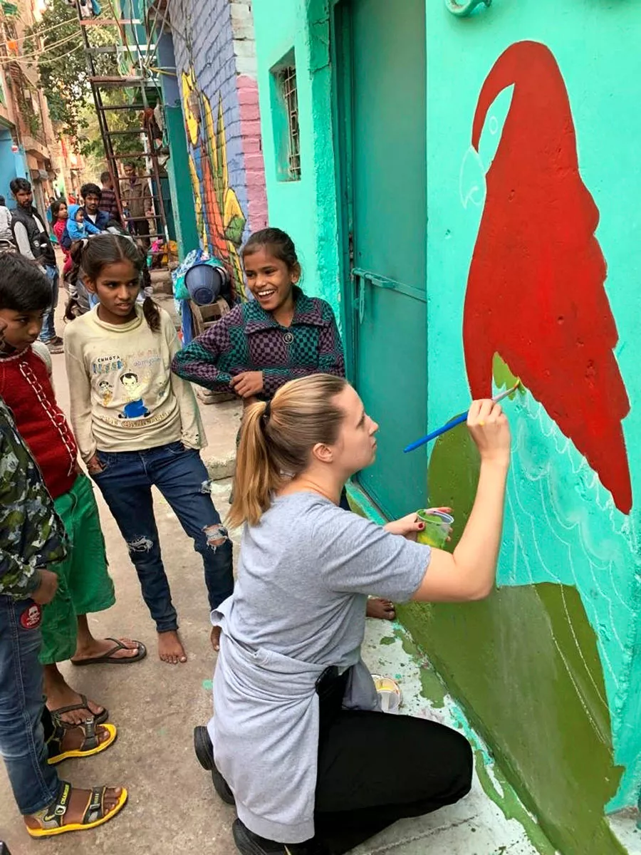 Nelli Mikkola maalaa talon seinää slummilasten kanssa New Delhissä.