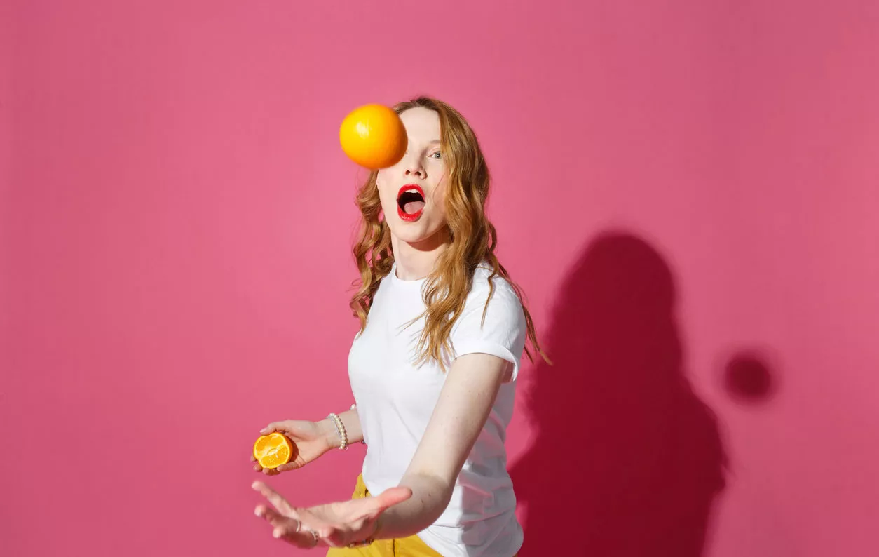 Nainen jonglööraa appelsiineilla.