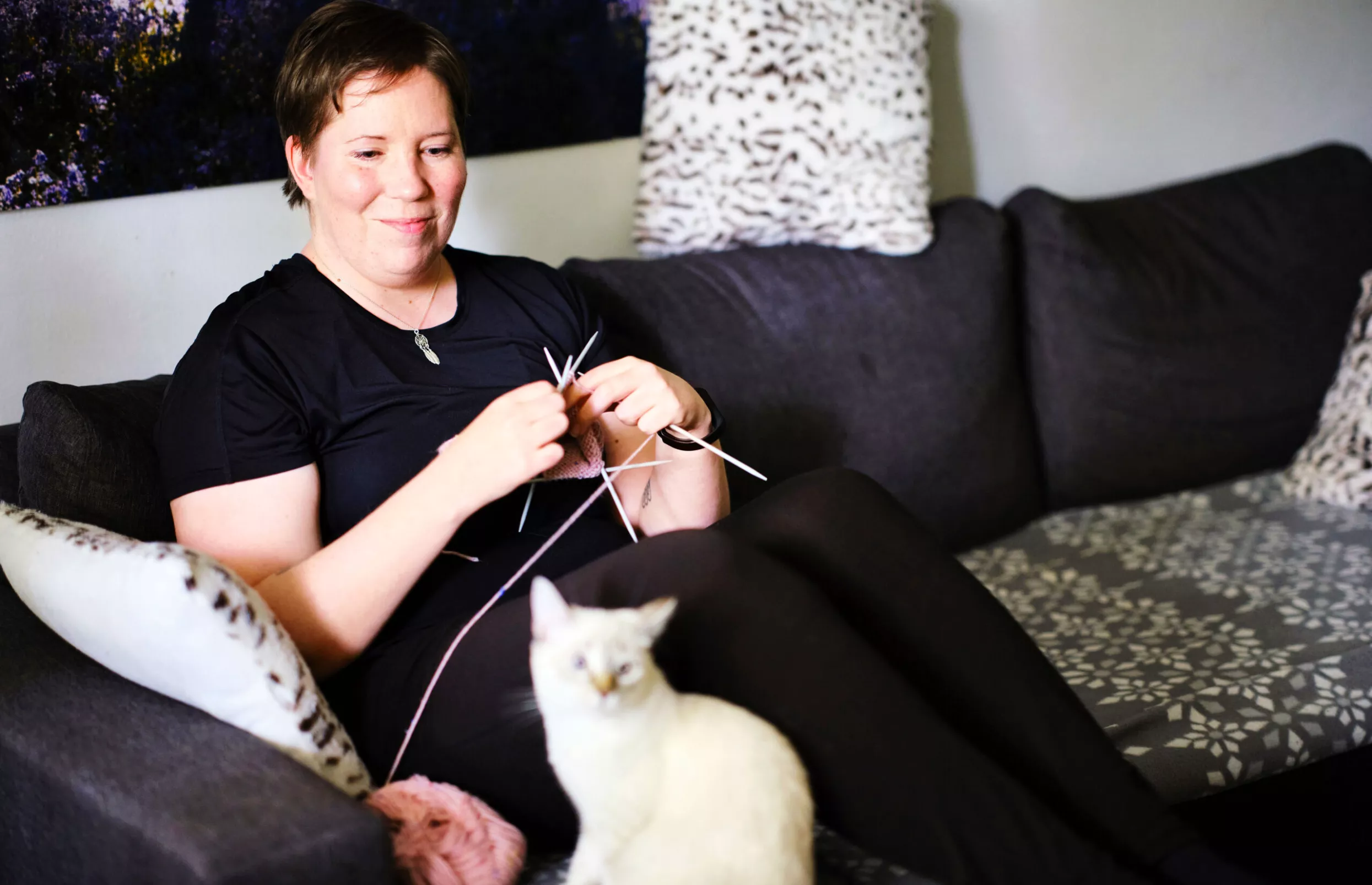 Long covidia sairastava Noora Aalto neuloo sohvalla, kissa istuu vieressä.