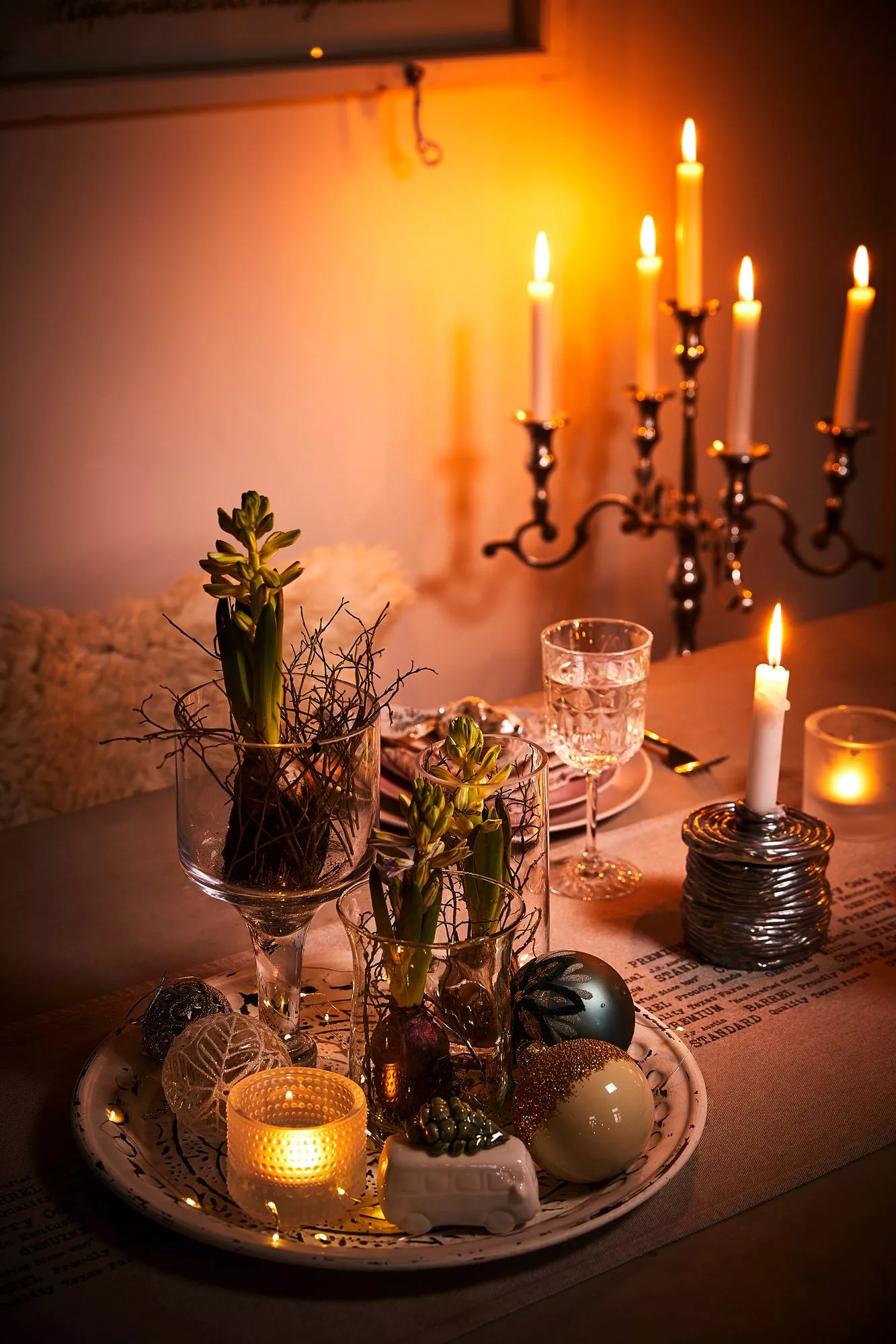 Jouluna Tuula kattaa pöytään kristallilasit ja paremmat lautaset. Kattauksen somisteena on laseihin istutettuja hyasintteja ja joulukuusen koristeellisia palloja. 