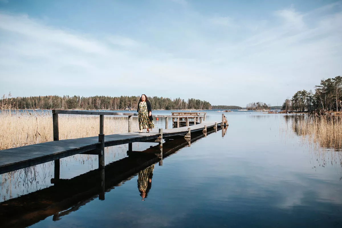 Kaisa Pöyhiä kävelee puista laituria pitkin järvimaisema taustallaan. 